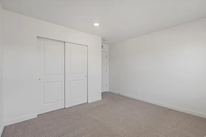 Spacious room featuring neutral carpeting, a pair of paneled sliding closet doors, white baseboards, and a recessed ceiling light