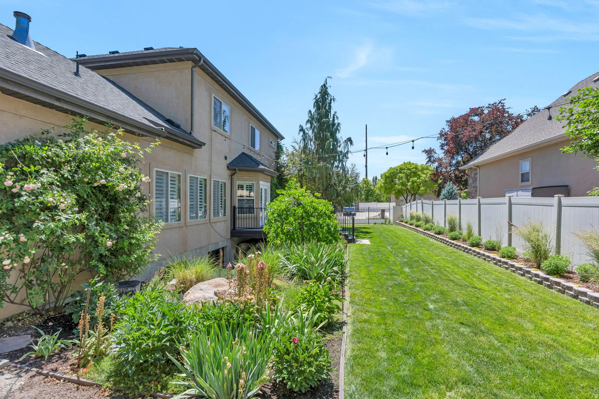 Spacious rear yard with a manicured lawn, established landscaping, and a white vinyl privacy fence