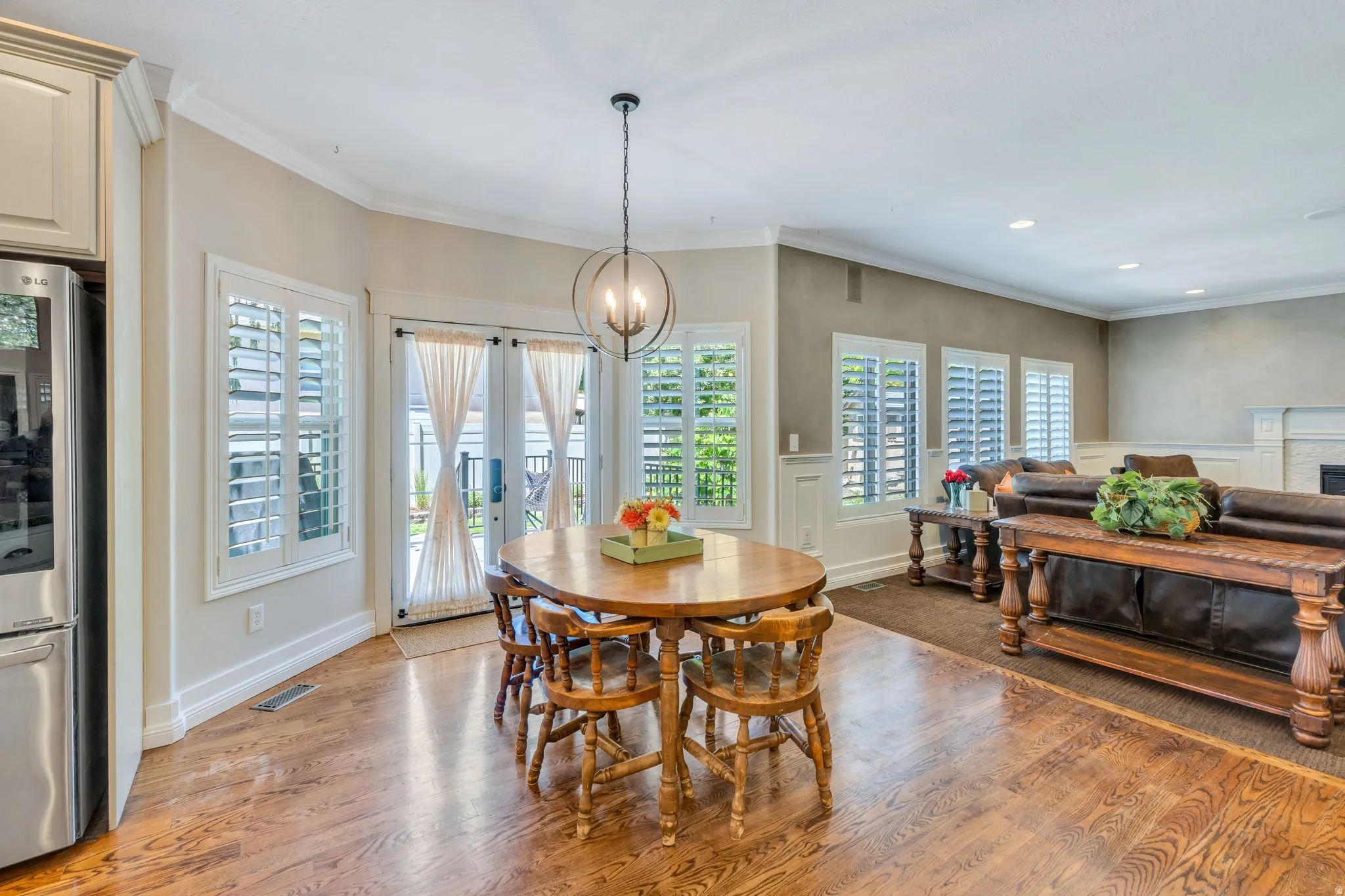 Open-concept living space featuring wood-finish flooring, white plantation shutters, crown molding, and a modern spherical chandelier