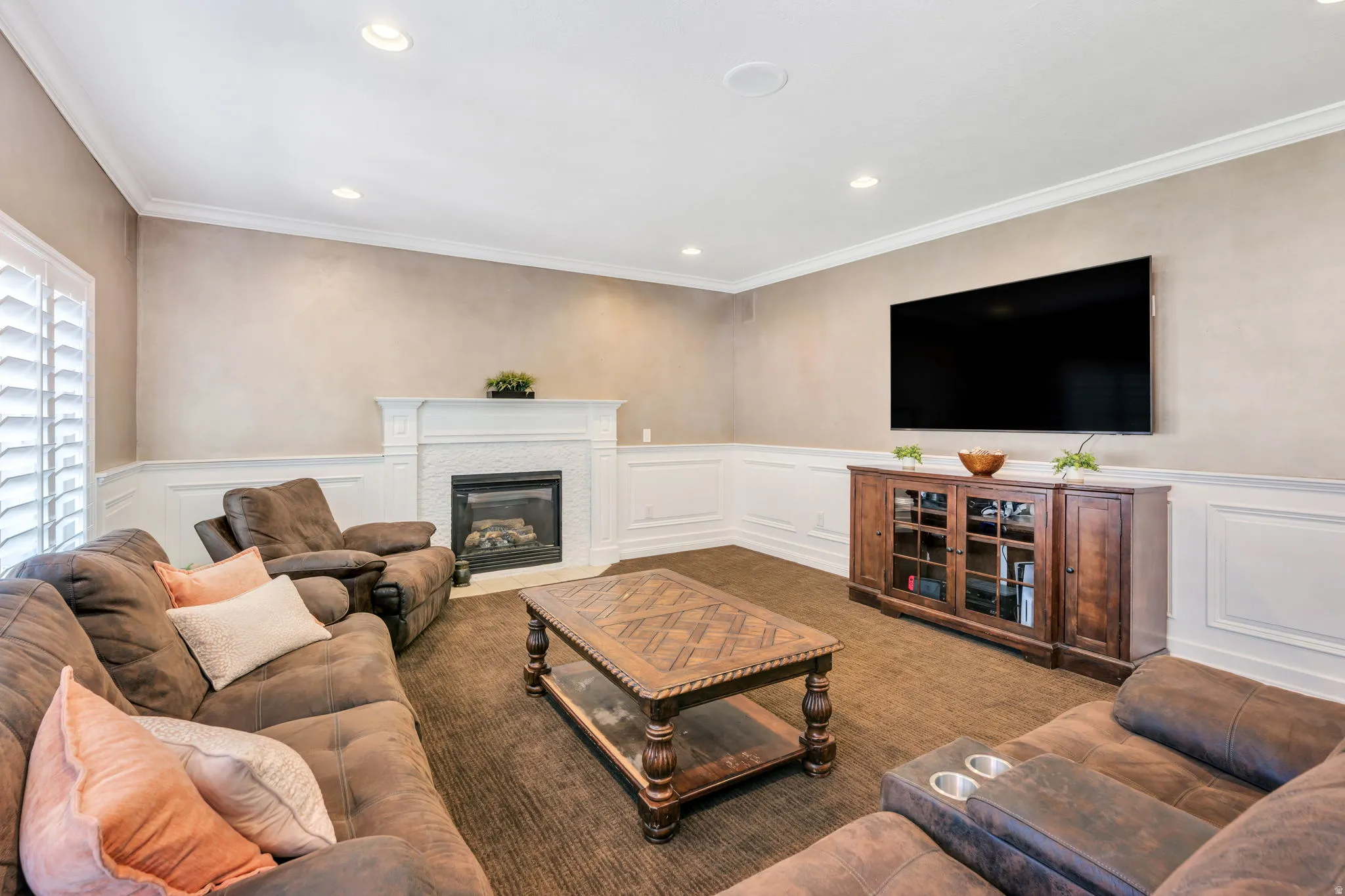 Living space featuring a fireplace with a detailed white mantel, white wainscoting, recessed lighting, and crown molding