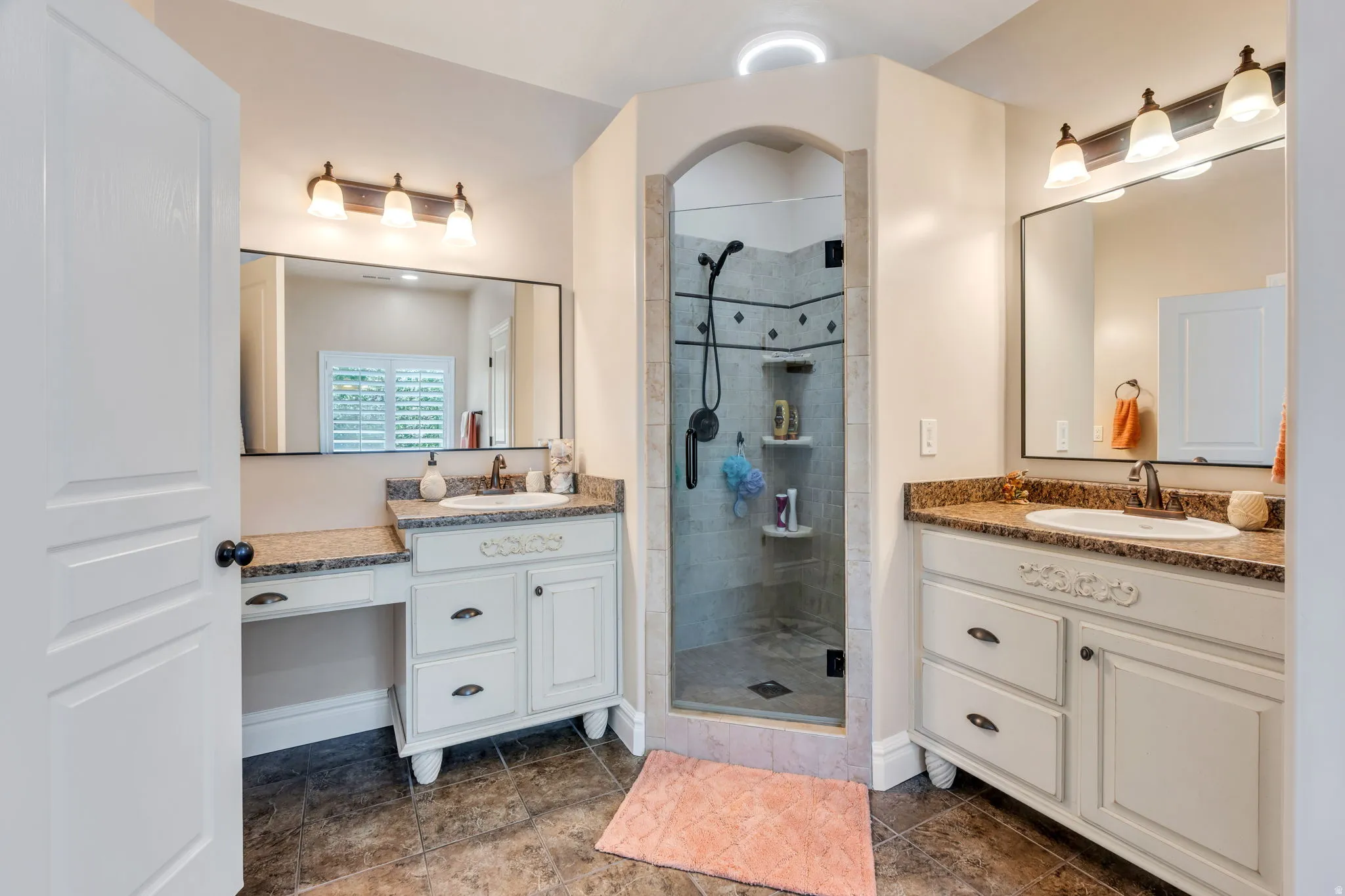 Bathroom featuring a tiled archway shower with glass enclosure, dual vanity sinks, and wood-finish flooring