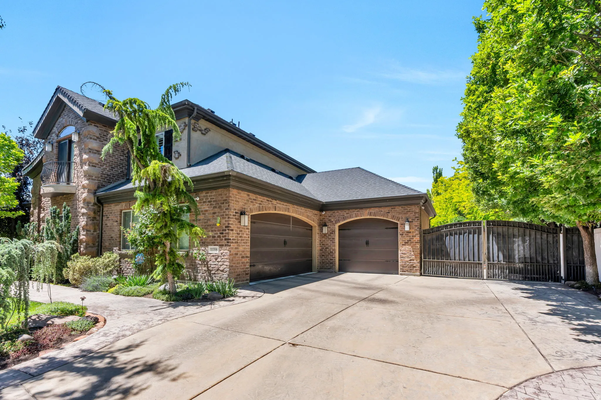 Brick and stone facade residence featuring a two-car garage with arched entrances, a paved driveway, and mature landscaping
