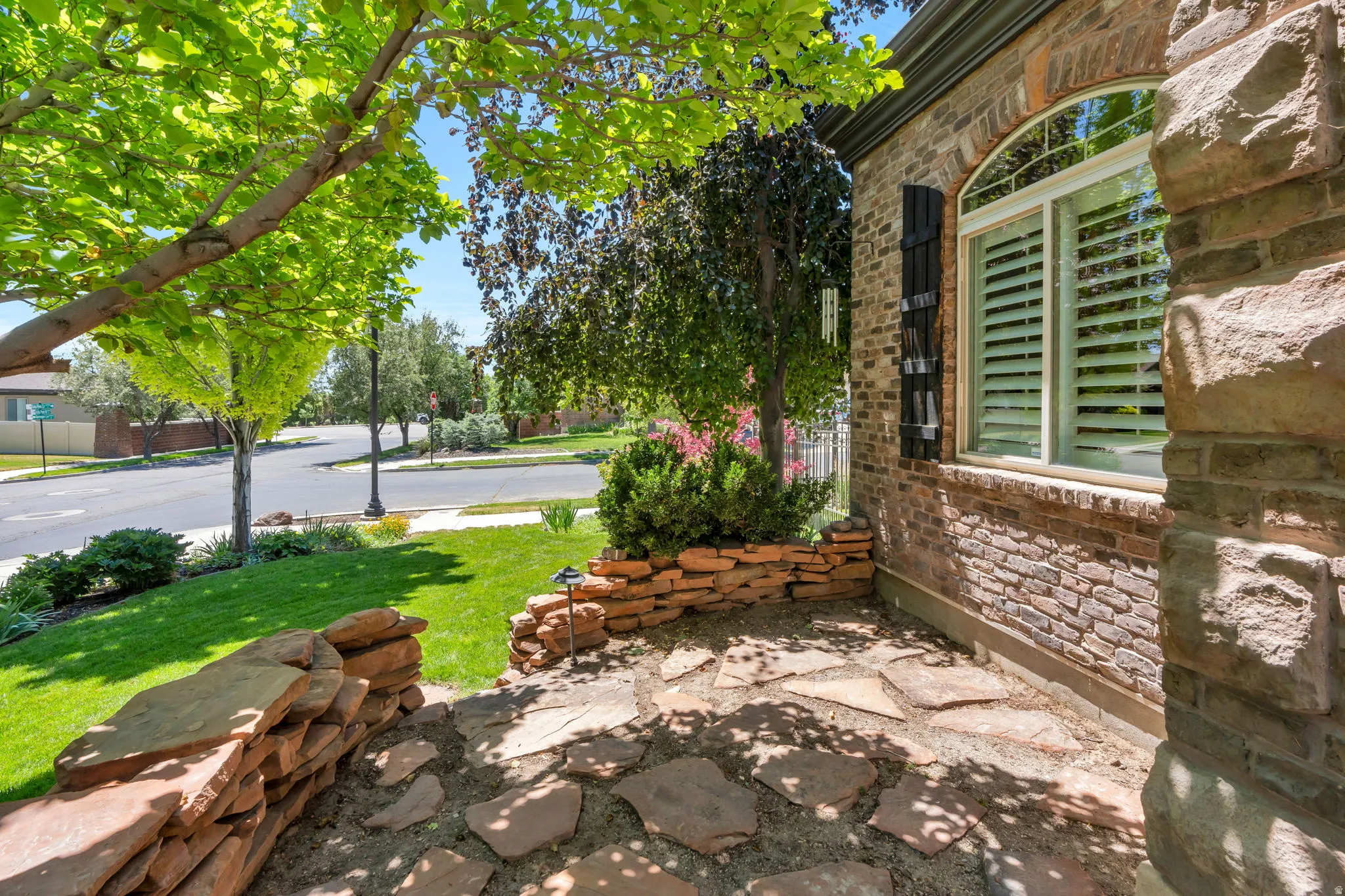 Stone and brick exterior featuring an arched window with white plantation shutters, a flagstone patio, and a manicured lawn