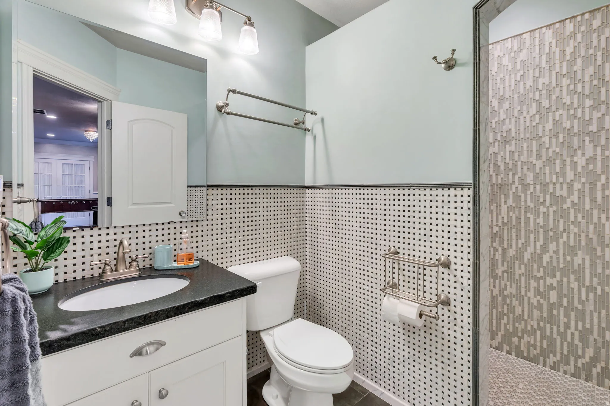 Bathroom featuring a white vanity with brushed nickel hardware, a dark countertop, an undermount sink, and a tiled shower enclosure with varied rectangular tiles