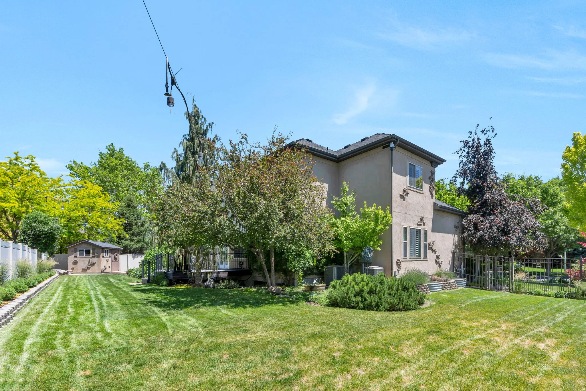 Expansive backyard featuring a manicured lawn, perimeter fencing, and mature trees