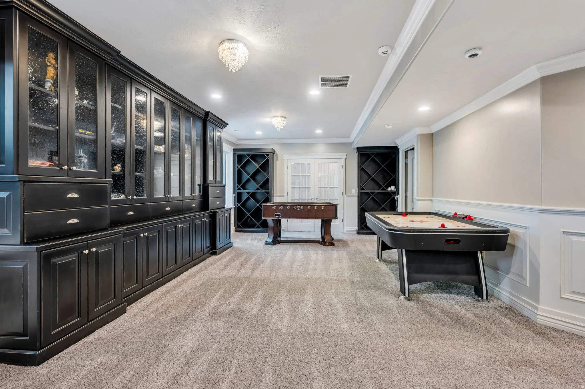 Extensive built-in black cabinetry with glass-front uppers and silver hardware, complemented by recessed lighting and two chandelier fixtures