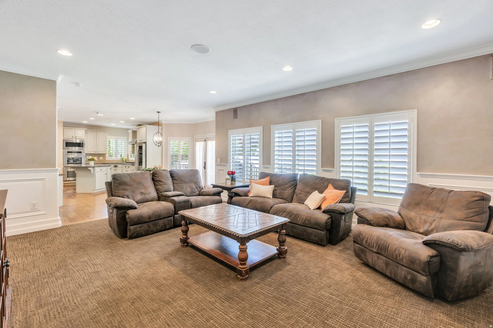 Spacious living area featuring neutral textured carpeting, recessed lighting, and white plantation shutters on multiple windows