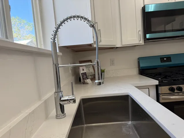 Modern kitchen featuring a stainless steel single-basin sink, a professional-style chrome faucet, white shaker-style cabinetry, and light-toned countertops