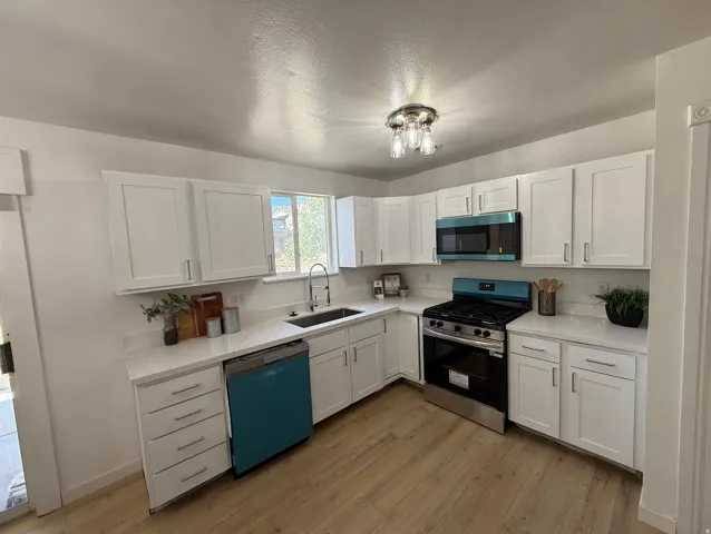 Modern kitchen featuring white shaker cabinetry, quartz countertops, wood-finish flooring, a stainless steel gas range, and integrated appliances