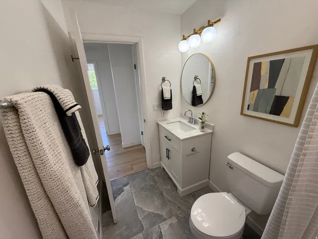 Bathroom featuring a white vanity with a light-colored countertop, an oval mirror, a three-light fixture with frosted globes, and slate-style floor tiling