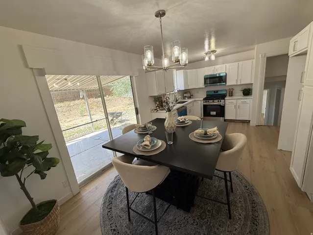 Open concept living space featuring wood-finish flooring, a contemporary dining fixture, and kitchen with white cabinetry
