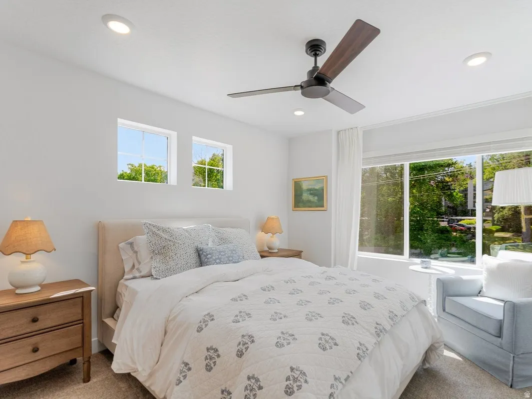 Bedroom featuring a large picture window with white drapery, two transom windows, a ceiling fan with integrated lighting, recessed lighting, and neutral carpeting