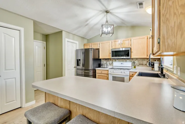 Kitchen featuring a breakfast bar with solid surface countertops, light wood-finish cabinetry, stainless steel microwave, and mosaic tile backsplash