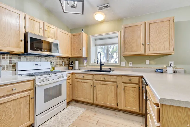 Kitchen featuring light wood cabinetry, stone-look countertops, and a mosaic tile backsplash