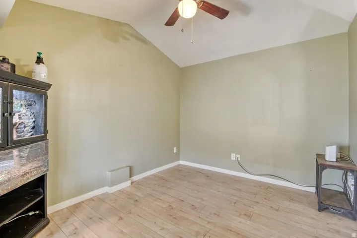 Vaulted ceiling featuring a ceiling fan with integrated lighting, light wood-finish flooring, and light green wall paint