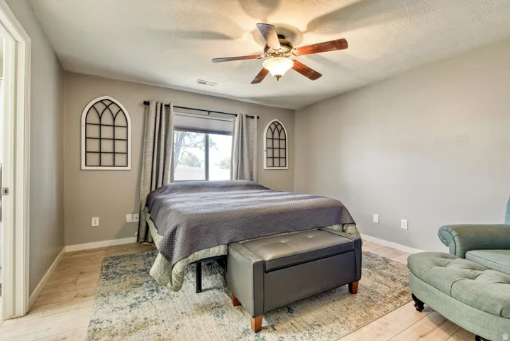 Bedroom featuring light wood-finish flooring, a ceiling fan with integrated lighting, and a window with roller shades and drapes