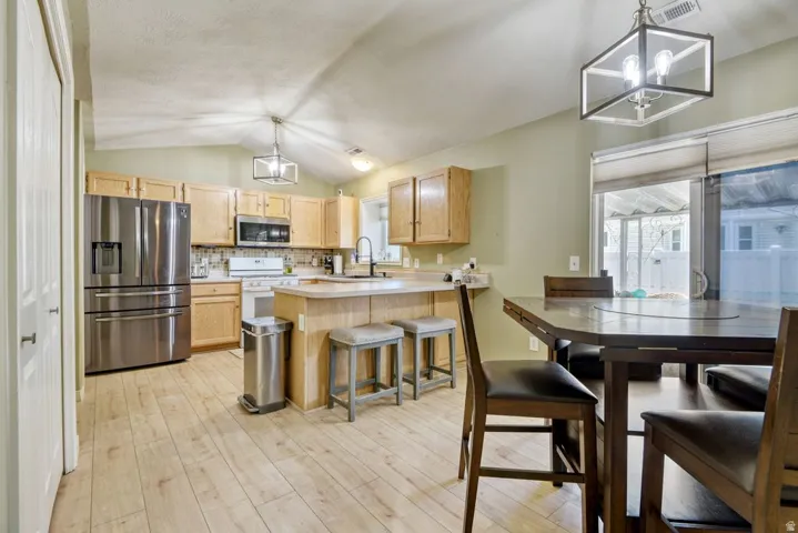 Kitchen and dining area featuring vaulted ceilings, wood-finish flooring, light-toned cabinetry, stainless steel appliances, and a breakfast bar