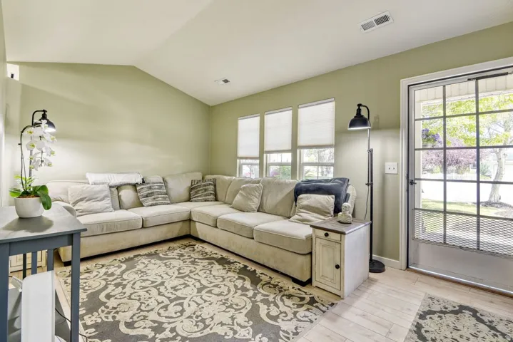 Living area featuring light-toned wood-finish flooring, a vaulted ceiling, and multiple windows with blinds