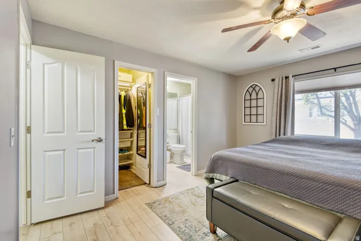 Bedroom featuring wood-finish flooring, a ceiling fan with integrated lighting, and a window with blinds and drapery
