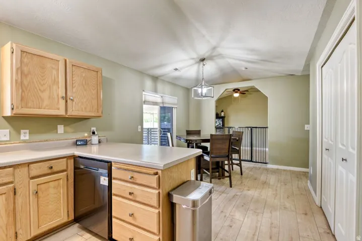 Kitchen and dining area featuring wood-finish flooring, light-toned cabinetry, a stainless steel dishwasher, and a contemporary ceiling light fixture