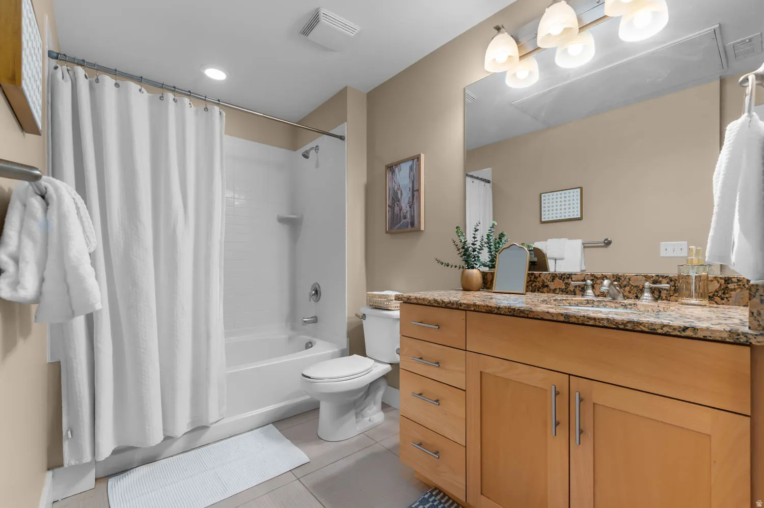 Bathroom featuring a light wood-finish vanity with ample storage, a granite-finish countertop, and a vanity mirror with a four-light fixture