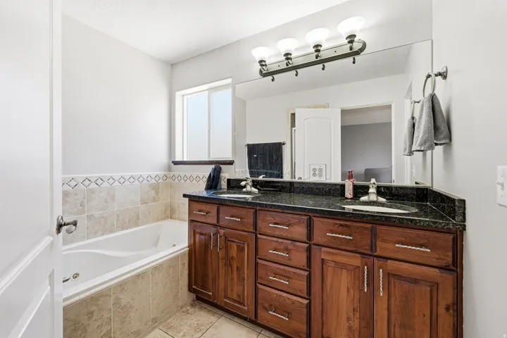 Bathroom featuring a spacious built-in tub with tile surround, a dual vanity with a dark countertop and two sinks, and a large wall-mounted mirror