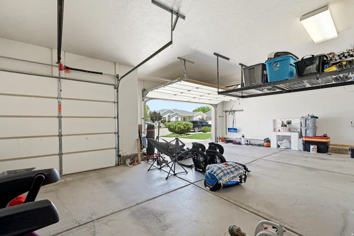 Spacious garage featuring a finished concrete floor, two overhead garage doors, a built-in storage shelf system, an overhead fluorescent light fixture, and a built-in workbench area