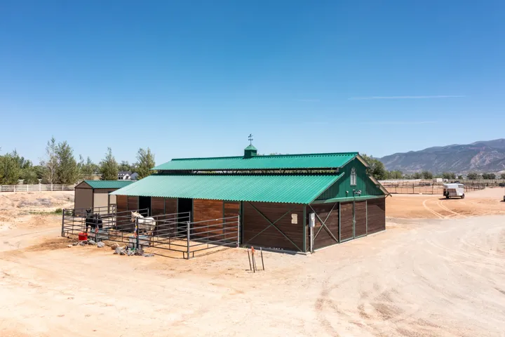 Barn structure featuring a green metal roof, wood-paneled siding, multiple stalls, and an attached shed