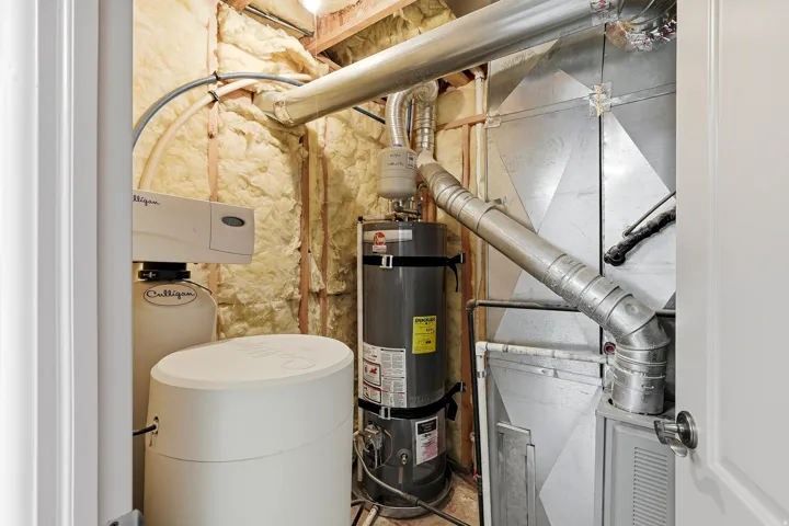 Utility closet featuring a water heater, water softener system, and exposed ductwork