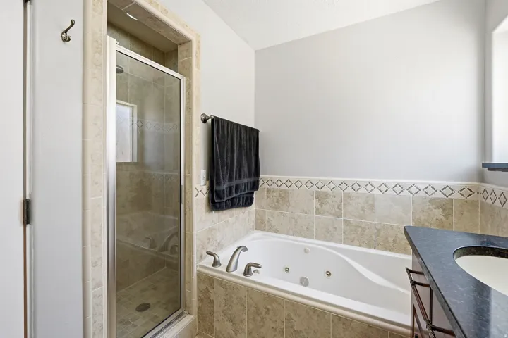 Bathroom featuring a built-in jetted tub, a separate glass-enclosed shower, a dark-toned vanity with a countertop sink, and tiled walls with decorative accents