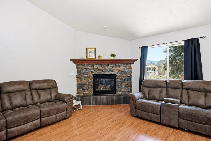 Living area featuring a stone-clad fireplace with a wood mantel, a tiled hearth, wood-finish flooring, and a large window with a mountain backdrop