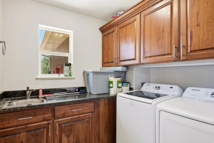 Laundry room featuring wood-finish cabinetry, a single basin sink with a chrome faucet, and a dark stone countertop