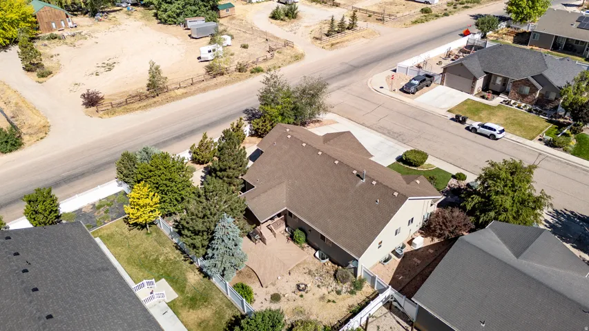 The property features a multi-level roofline with a brown shingle roof, a spacious paved patio, and mature trees providing natural landscaping