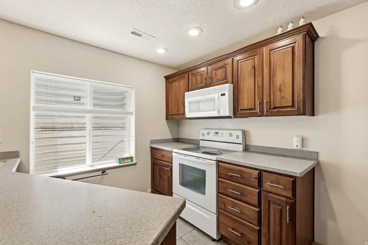 Functional kitchen featuring wood-finish cabinetry, light-toned countertops, a white electric range, and a built-in white microwave