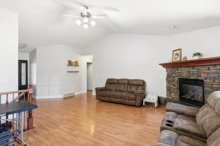Spacious living area featuring vaulted ceilings, wood-finish flooring, and a stone-faced fireplace with a wood mantel