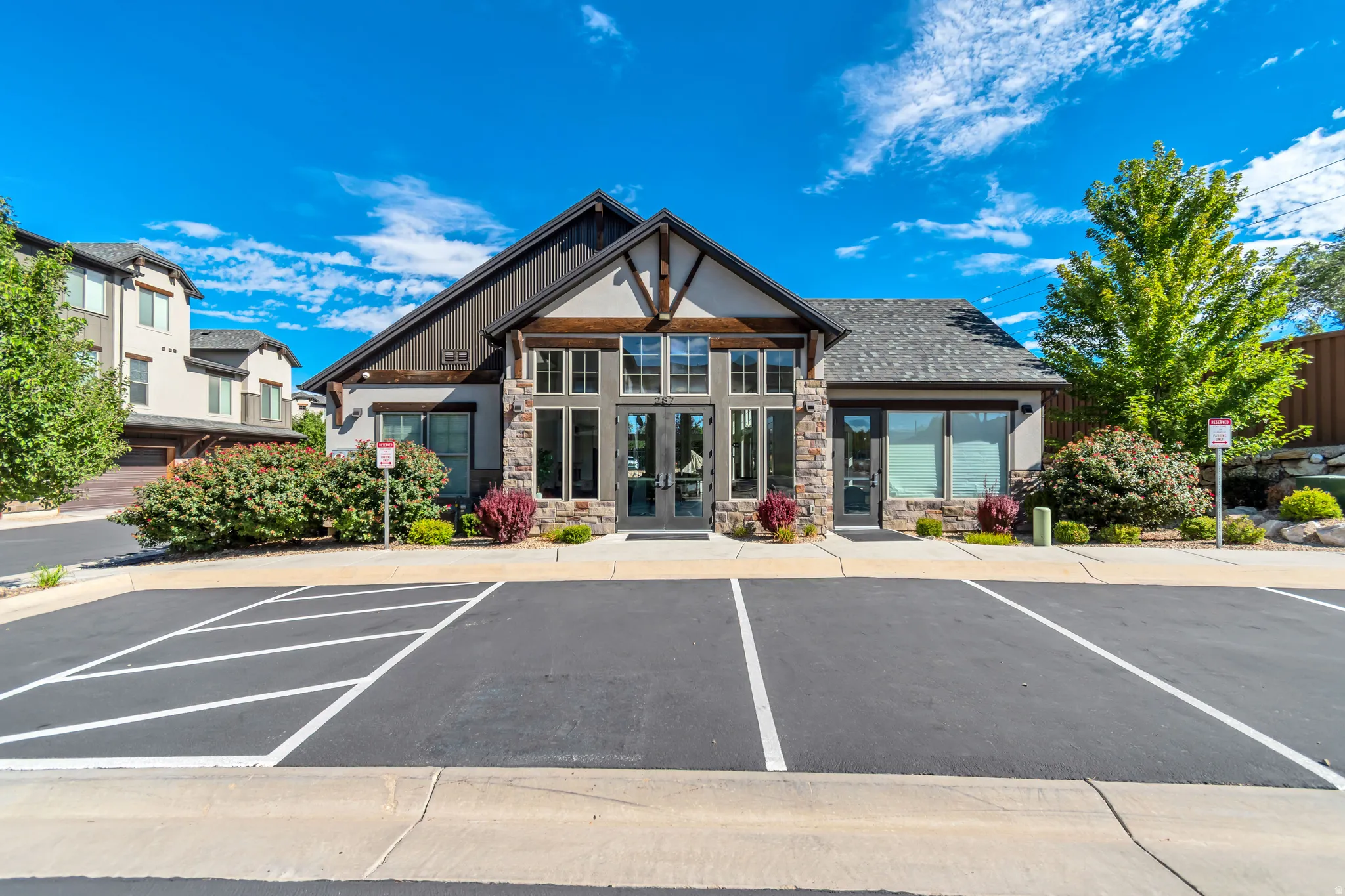 Stone and stucco exterior with multiple large windows, a prominent gable roofline, and a paved parking area