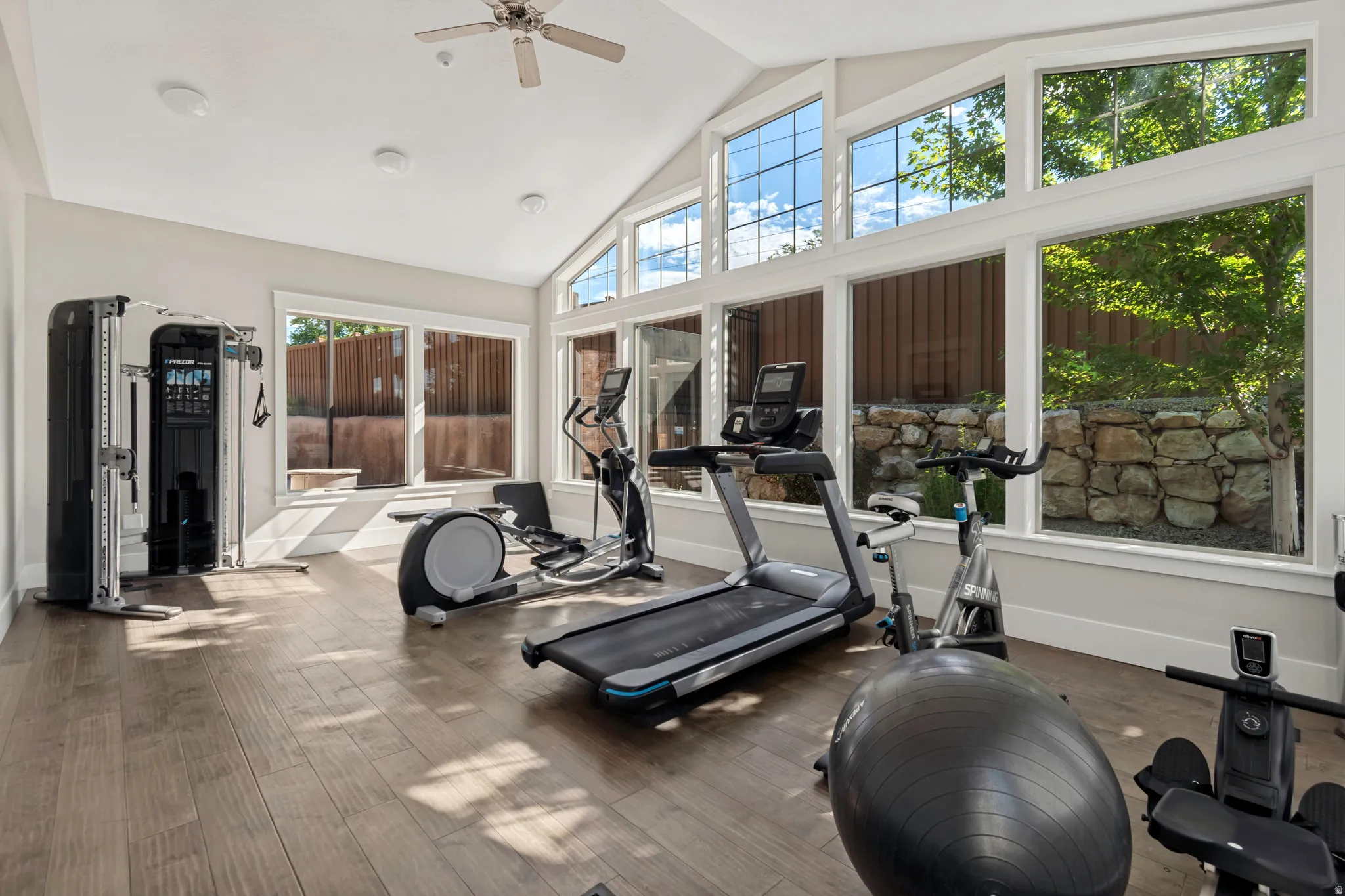 Room featuring a vaulted ceiling with a ceiling fan, wood-finish flooring, and expansive windows