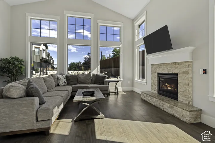 Vaulted ceiling, wood-finish flooring, stone-clad fireplace, white mantel, and multiple large windows