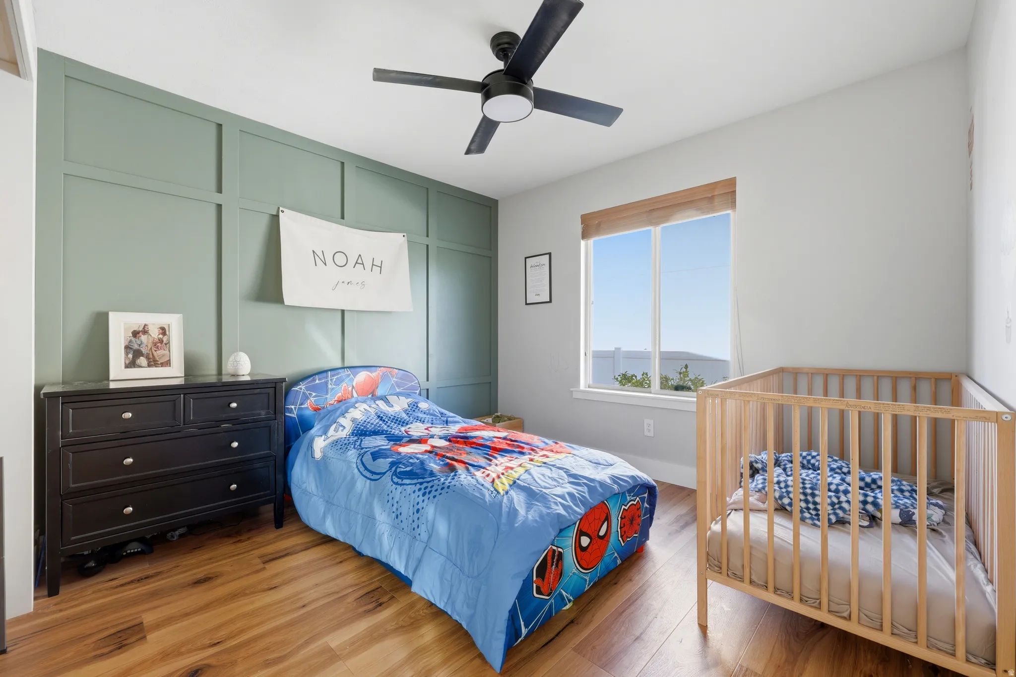 Room featuring wood-finish flooring, a decorative accent wall with paneling, and a ceiling fan