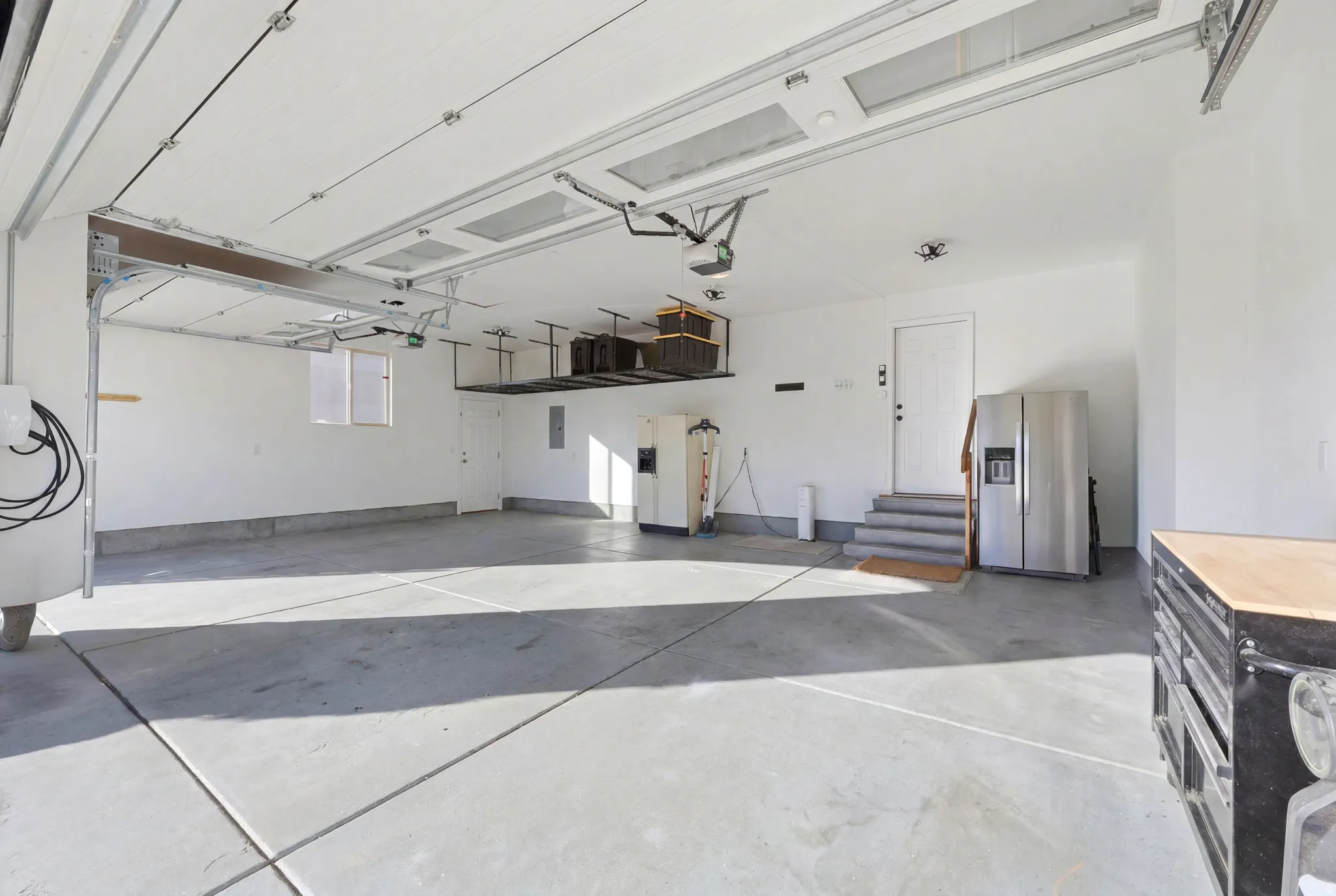 Spacious concrete-floored garage featuring a white overhead door, built-in overhead storage racks, an interior access door, and a dedicated window