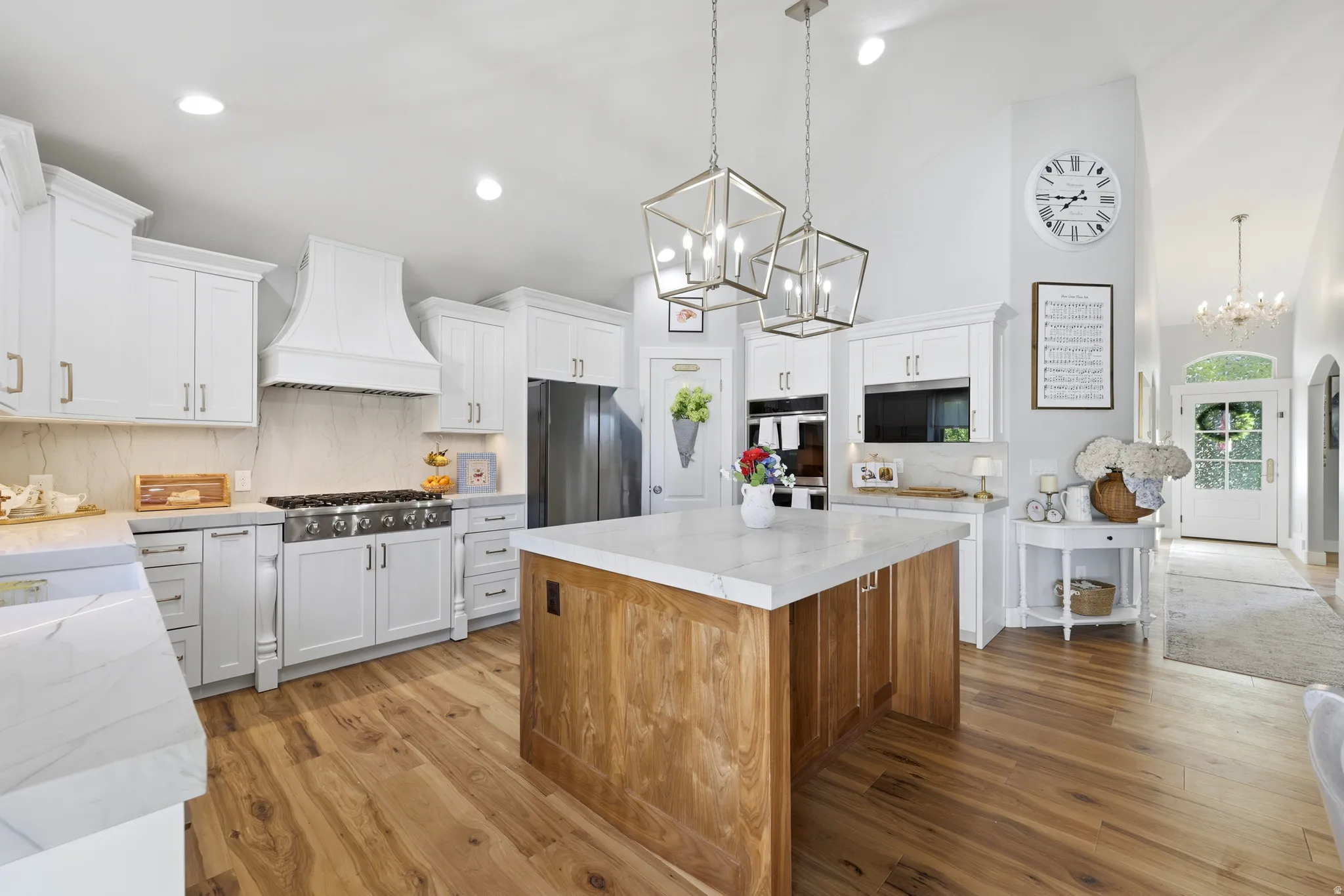 Gourmet kitchen featuring a wood-finish island with a light-toned countertop, white cabinetry, a large range with custom hood, and stainless steel appliances