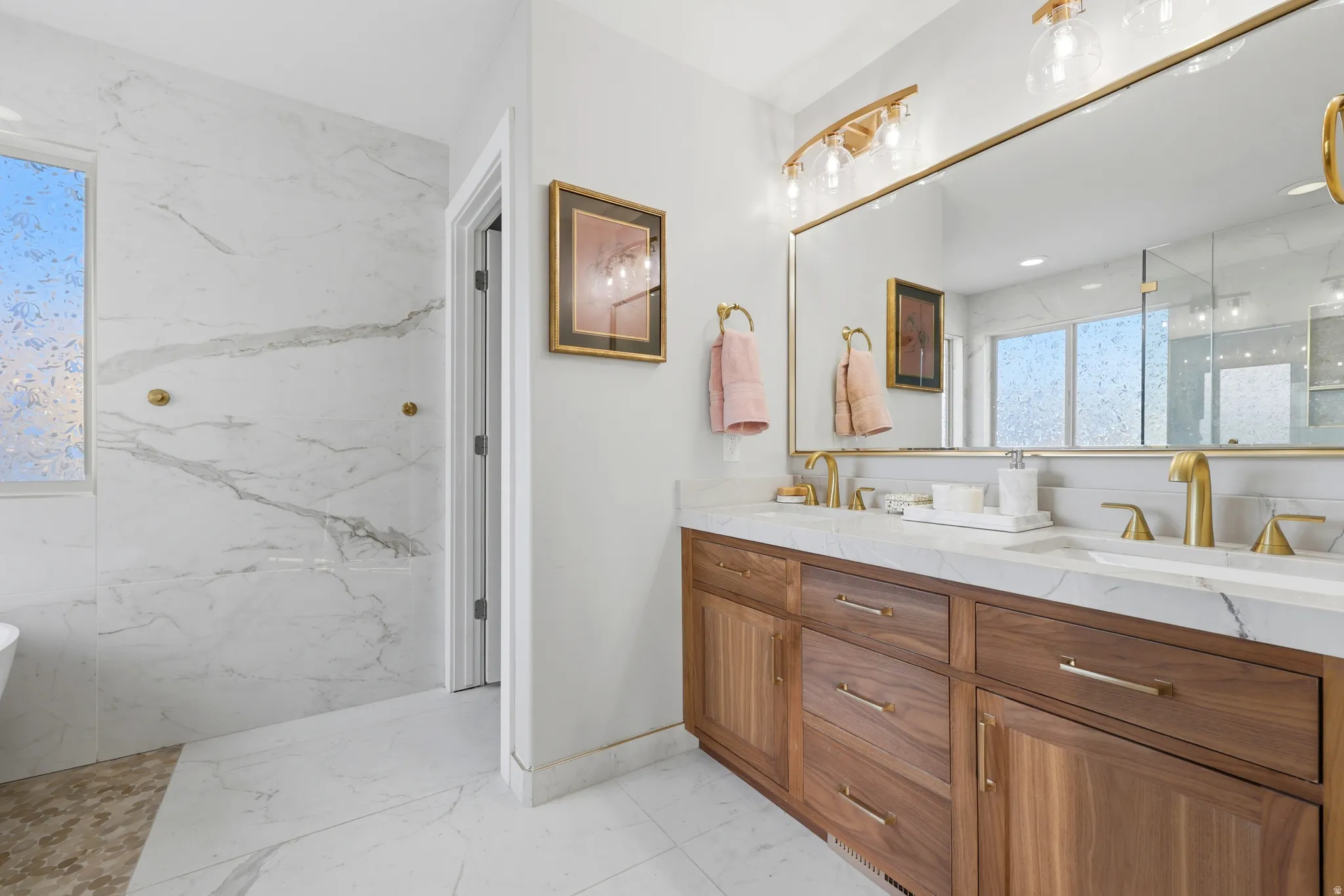 Double vanity featuring wood-finish cabinetry, white stone countertops, and gold-finish fixtures