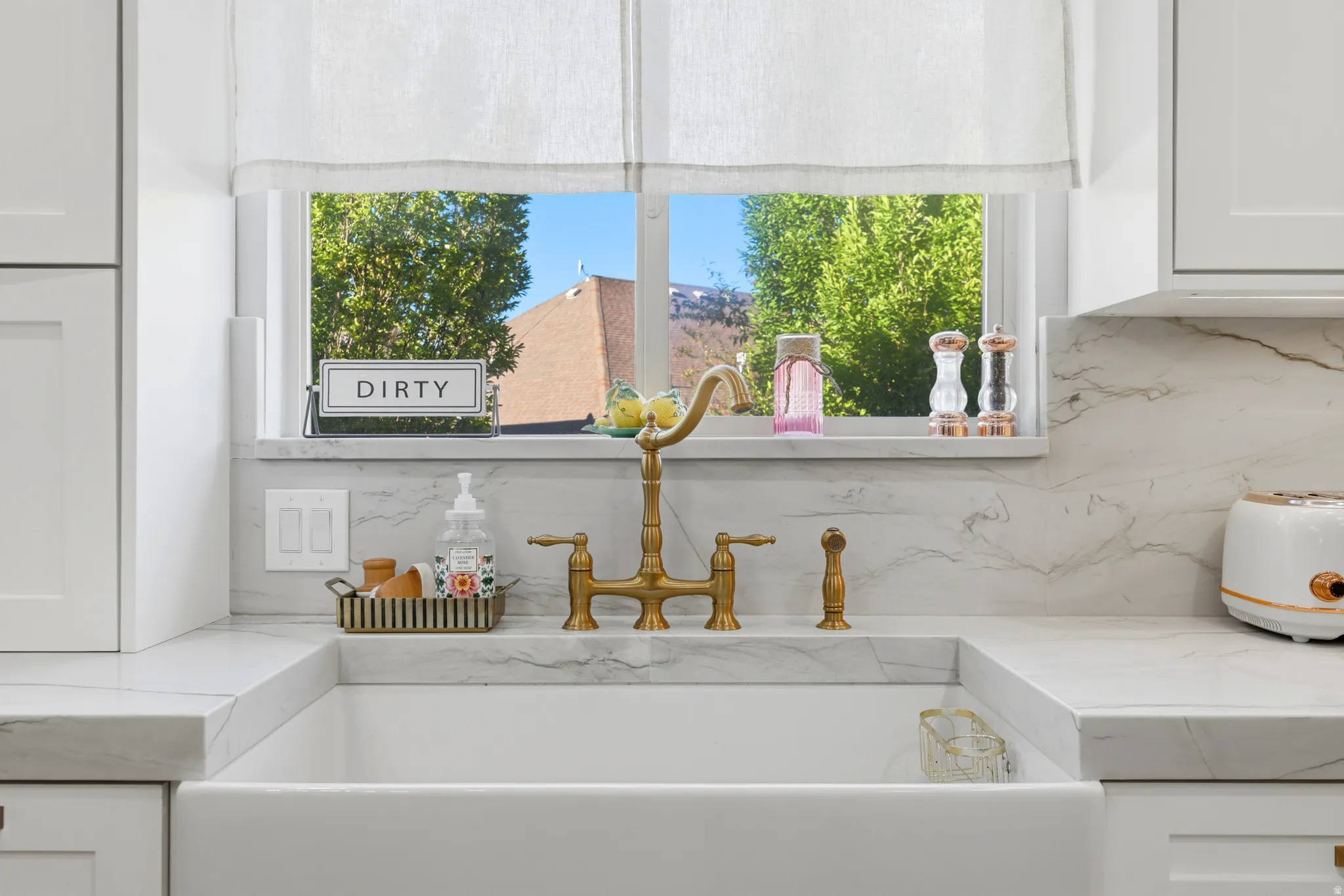 Kitchen featuring a white apron-front sink, a brass-tone bridge faucet, light stone countertops, and a matching stone backsplash with subtle veining