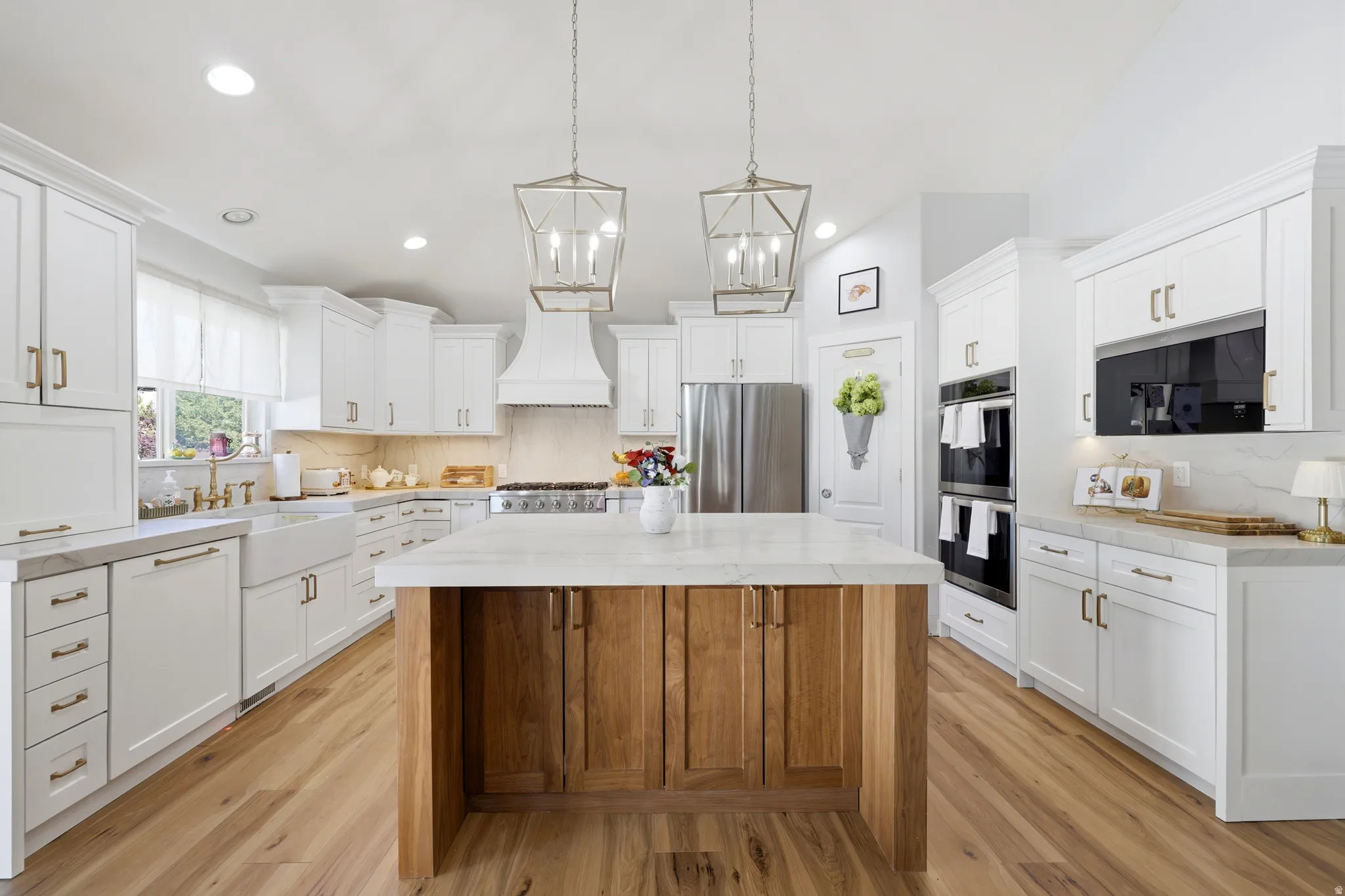 Bright kitchen featuring a substantial wood-finish island with a light-toned countertop, extensive white cabinetry, stainless steel appliances, and wood-finish flooring throughout