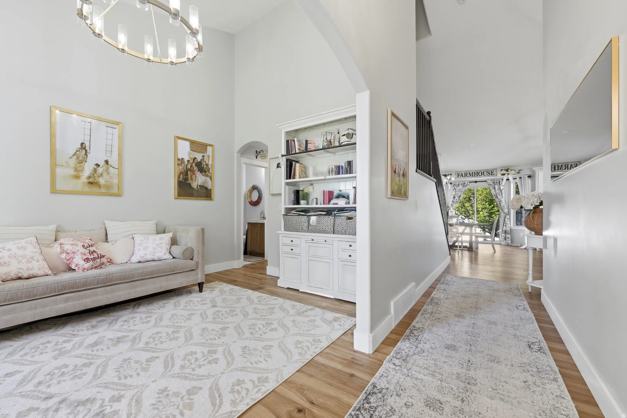 Vaulted ceilings with a contemporary chandelier, light wood-finish flooring, and a built-in white shelving unit with cabinet storage