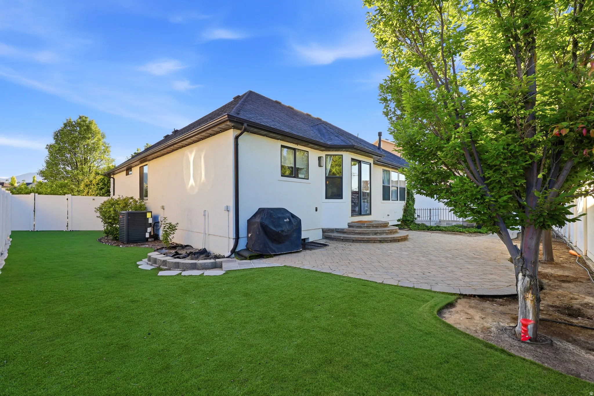 Spacious backyard with a paved patio, an artificial turf lawn, and a mature tree