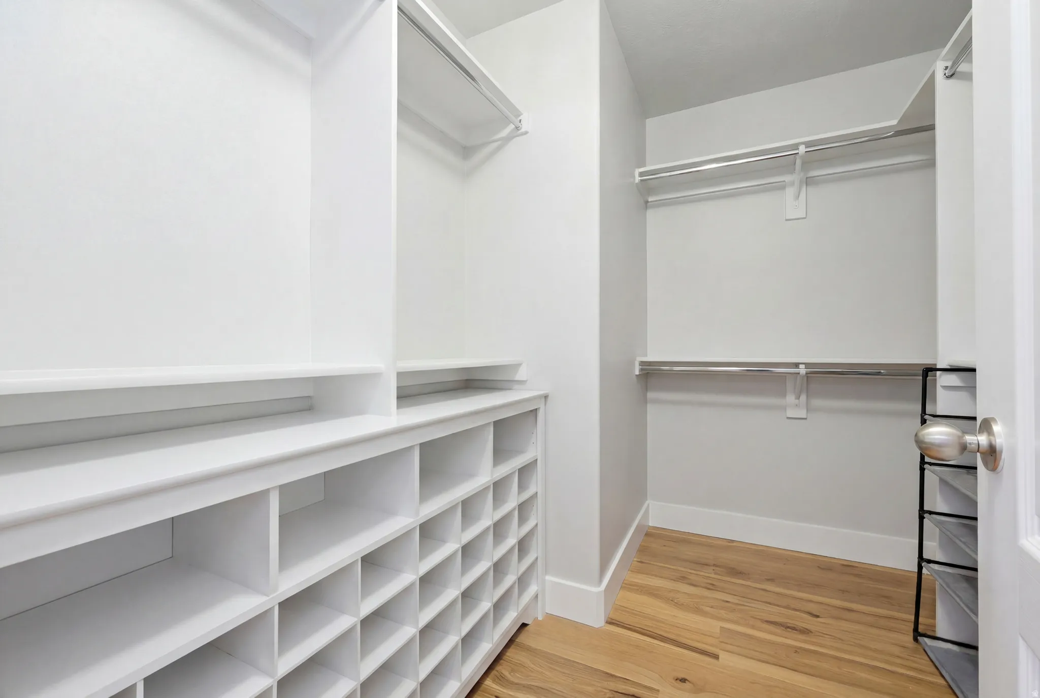 Spacious walk-in closet featuring extensive built-in shelving, shoe cubbies, multiple hanging rods, and wood-finish flooring
