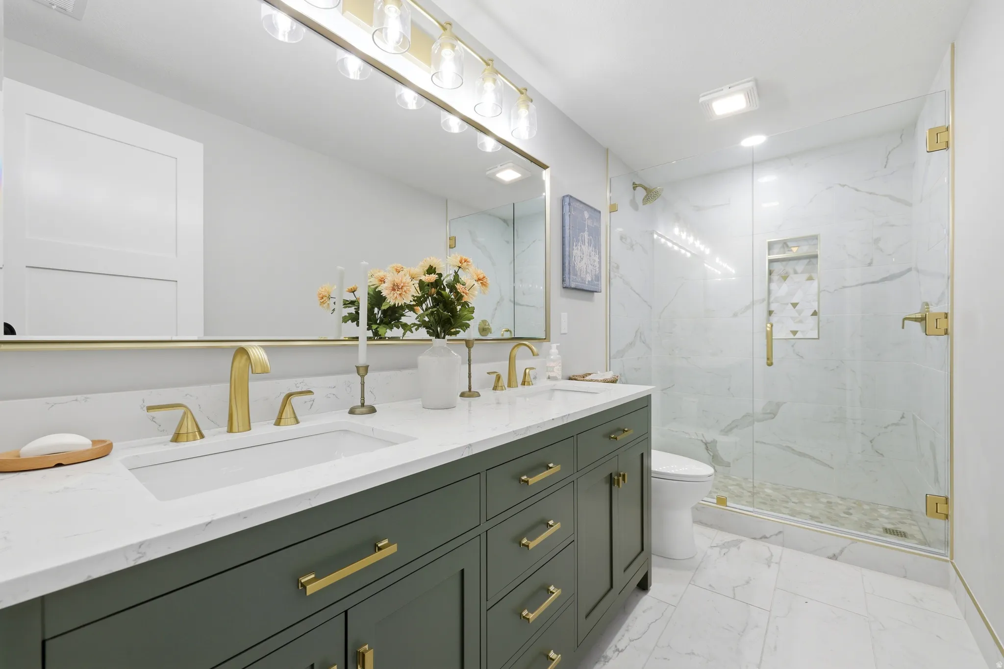 Spacious bathroom featuring a dual-sink vanity with a white countertop and green cabinetry, undermount sinks, and gold-finish fixtures