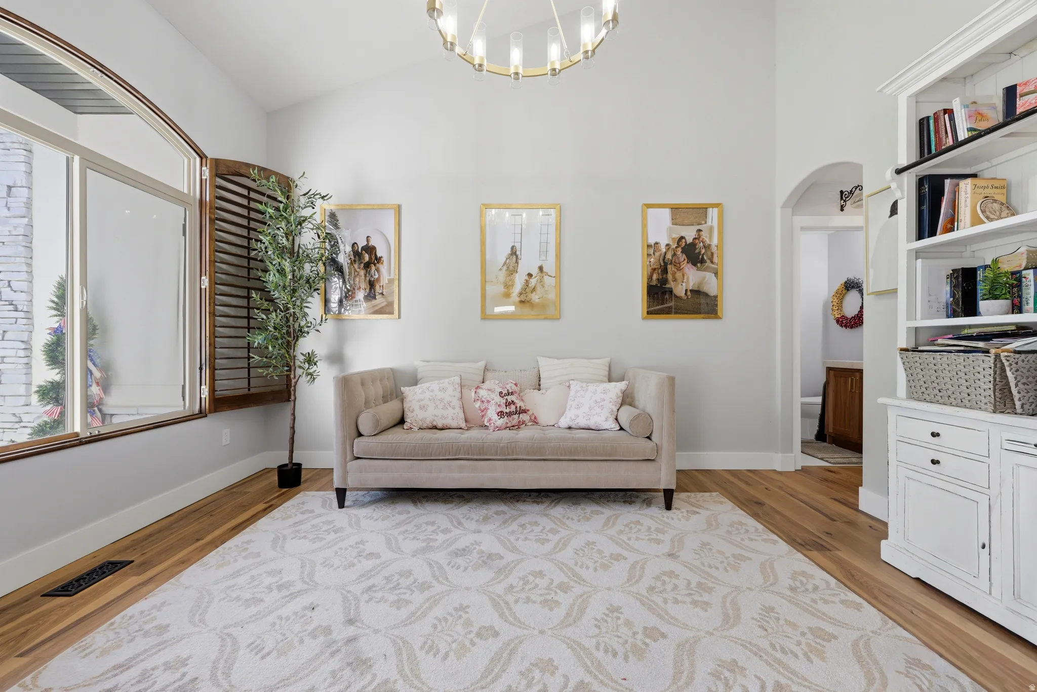 Vaulted ceiling featuring a circular chandelier, hardwood flooring, and an arched window with wooden shutters