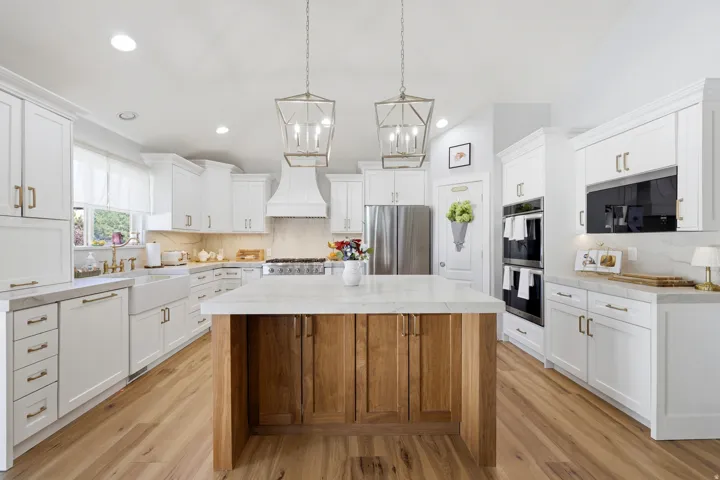 Spacious kitchen featuring an expansive wood-finish island, white shaker cabinetry, stainless steel appliances, dual wall ovens, and a farmhouse sink